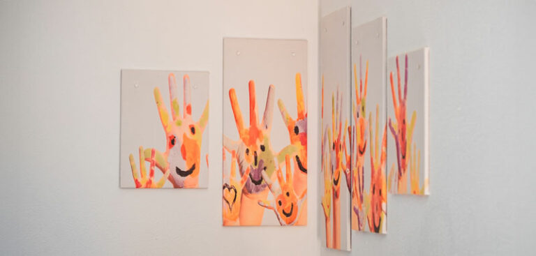 Eine Sammlung farbenfroher Handabdruck-Gemälde auf einer weißen Wand, die glückliche Gesichter und Herzen zeigen.