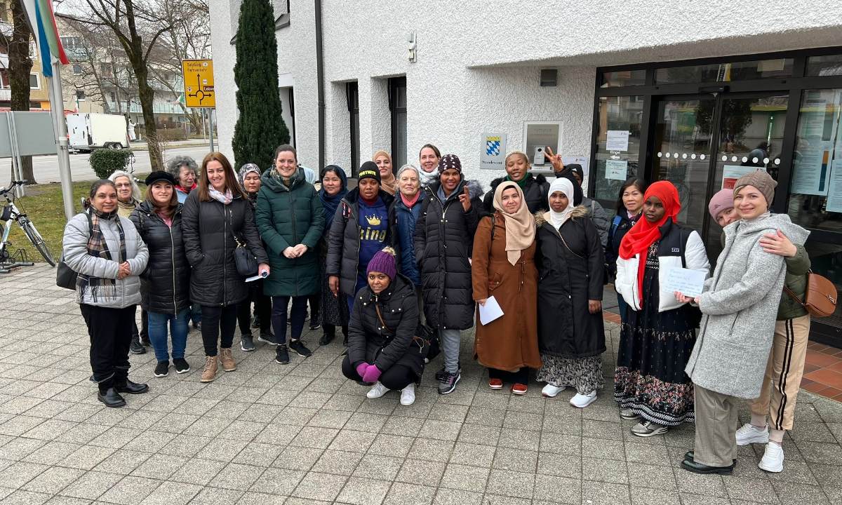 Eine Gruppe von Frauen steht vor einem Rathausgebäude, lächelt in die Kamera und wirkt gut gelaunt an einem kühlen Tag.