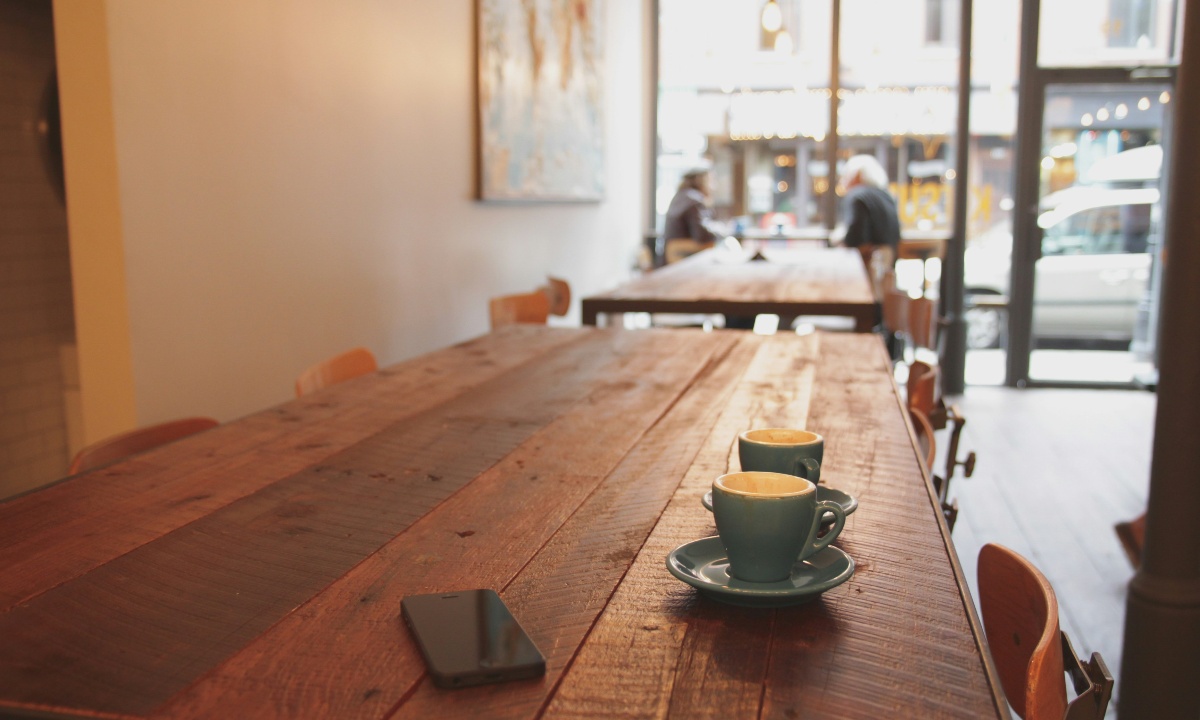 Zwei blaue Kaffeetassen und ein Smartphone auf einem Holztisch in einem Café.