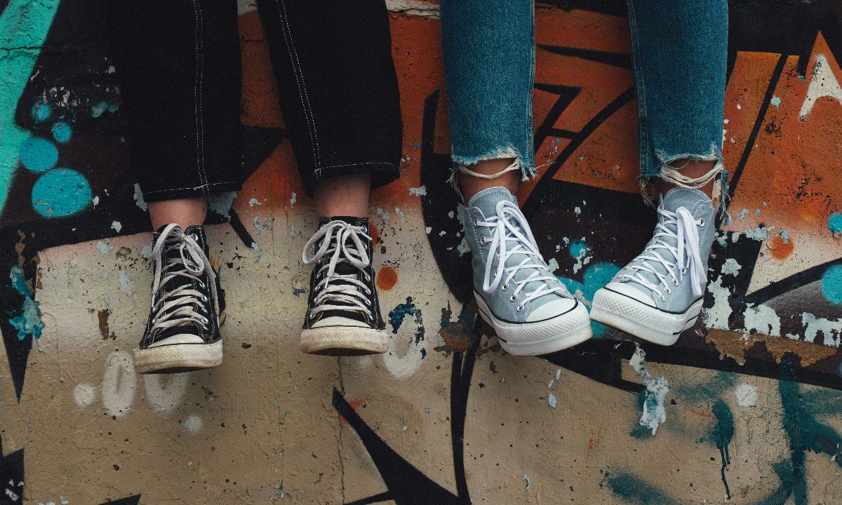 Ein Paar schwarze und ein Paar weiße High-Top-Sneaker stehen auf einer Graffitiwand.
