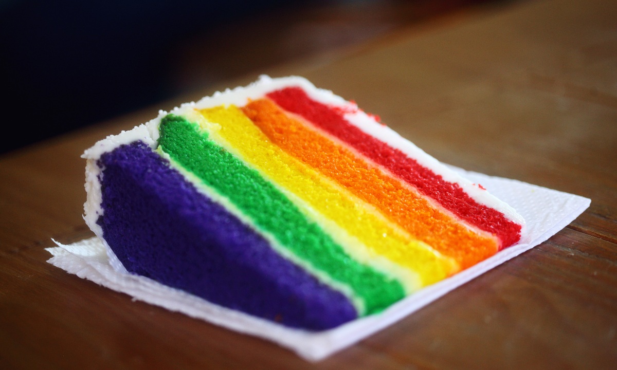Ein Stück Regenbogenkuchen mit Schichten aus lila, grünem, gelbem, orangefarbenem und rotem Teig.