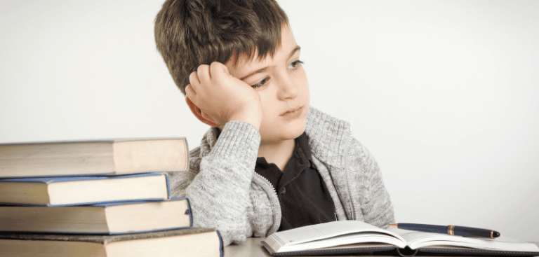 Kind schaut gelangweilt zur Seite. Vor ihm liegen Bücher