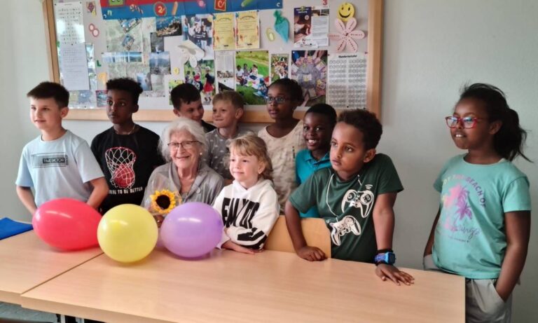 Mehrere Kinder und eine Erwachsene Person stehen um einen Tisch. Auf dem Tisch liegen Luftballons