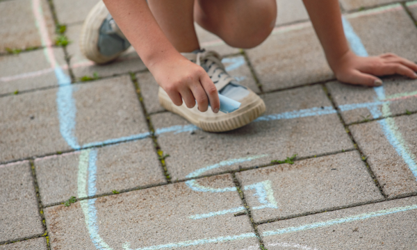 Sportkinderhaus Kreidekästchen Ein Kind malt mit Kreise ein Hüpfkästchen auf Steinplatten am Boden.