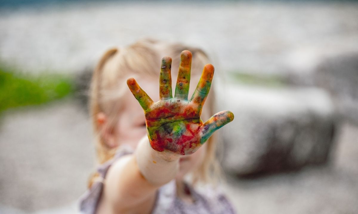 Akademie KITAS Ein Mädchen, das eine bunt bemalte Kinderhand zeigt